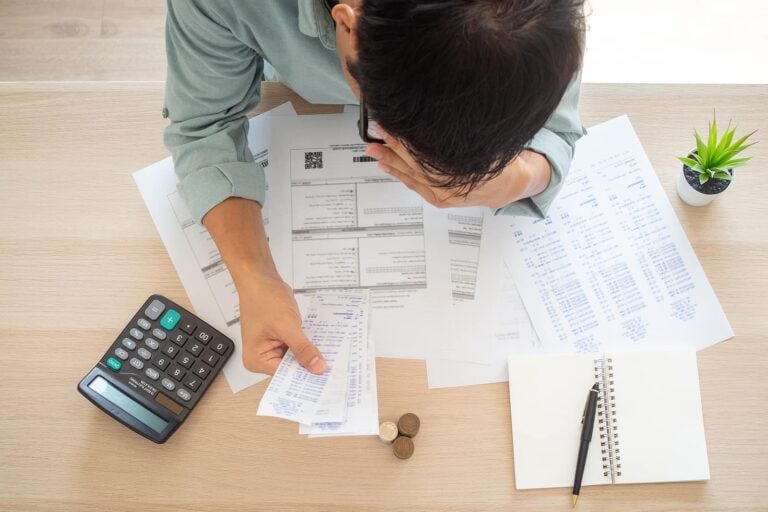 A business owner worried hands touch forehead which has many expenses such as electricity bills, internet bills, mobile phone bills and credit card bills on hand, no money to pay