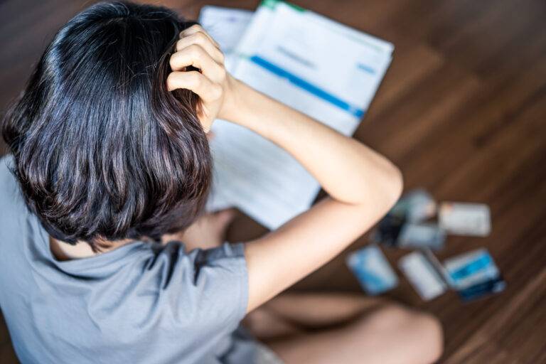 Top view of stressed young Asian woman hands holding the head trying to find money to pay credit card debt and all loan bills. Financial problem from coronavirus or covid-19 outbreak crisis concept