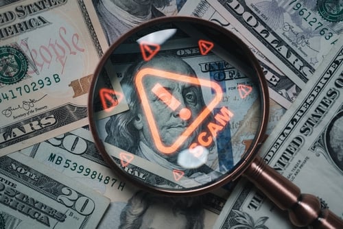 magnifying glass over money with scam alert on magnifying glass