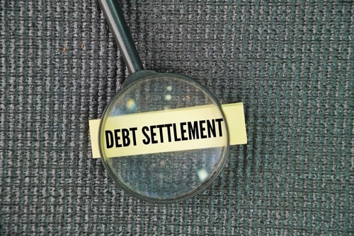 magnifying glass with debt settlement note under