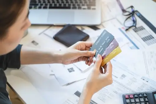 woman holding three credit cards in her hands while she looks down at them over a table of paperwork