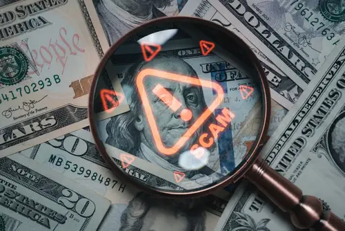 magnifying glass over money with scam alert on magnifying glass